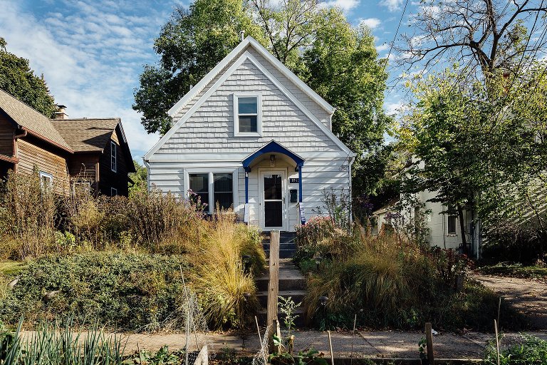 White house with triangle peak, large front yard garden & blue skies 