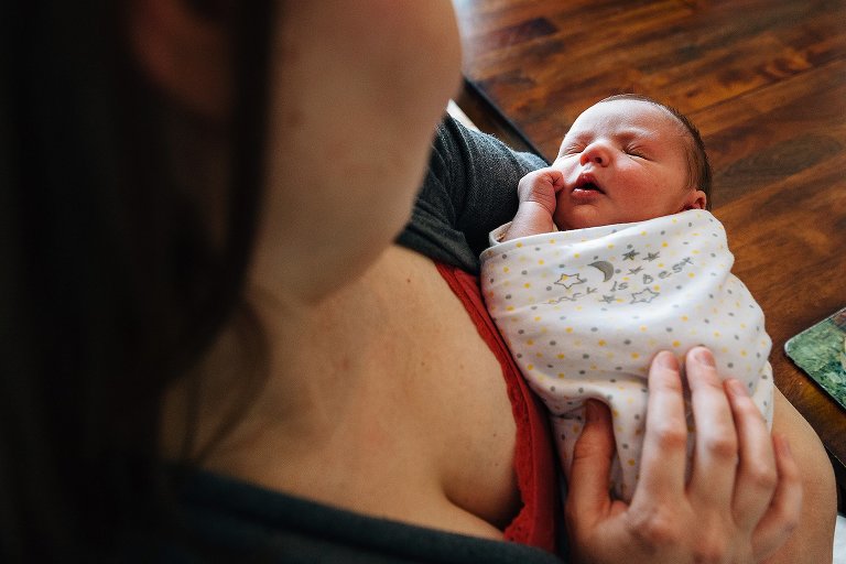 Sleeping newborn squints eyes tightly while being held by his mother. 