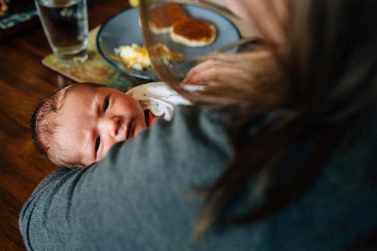 Calm, alert newborn in mother's arms. View of untouched breakfast food on table behind them. 