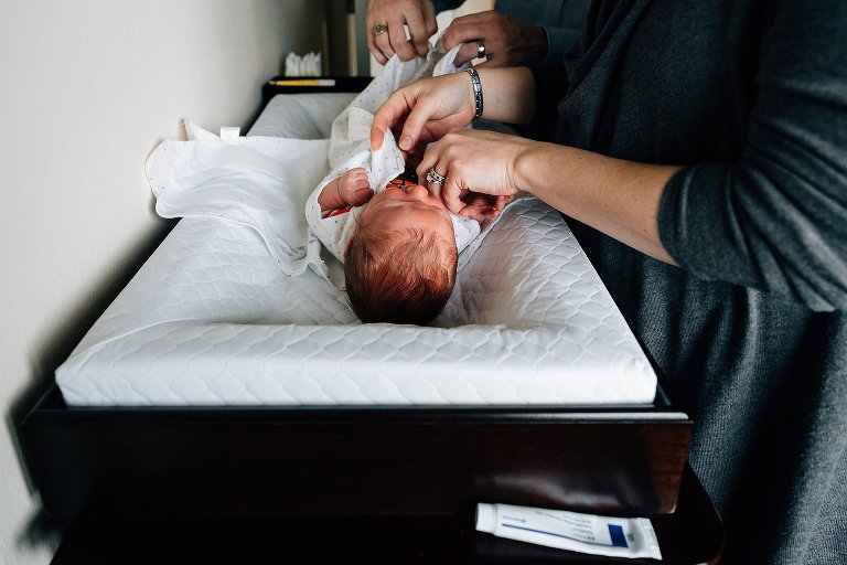 Boht mom and dad unswaddle and prepare to change newborn baby on a changing table. 