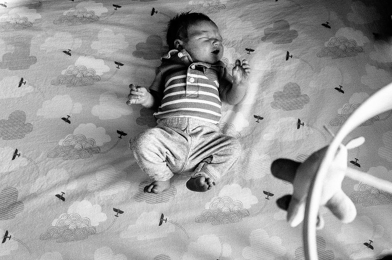 Black and white. Top down view of newborn lying in crib, eyes closed but newborn startle effect. 