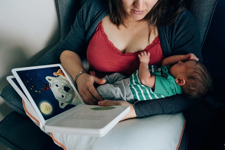 Mom holds sleeping baby in arms while she reads a children's board book to him. 