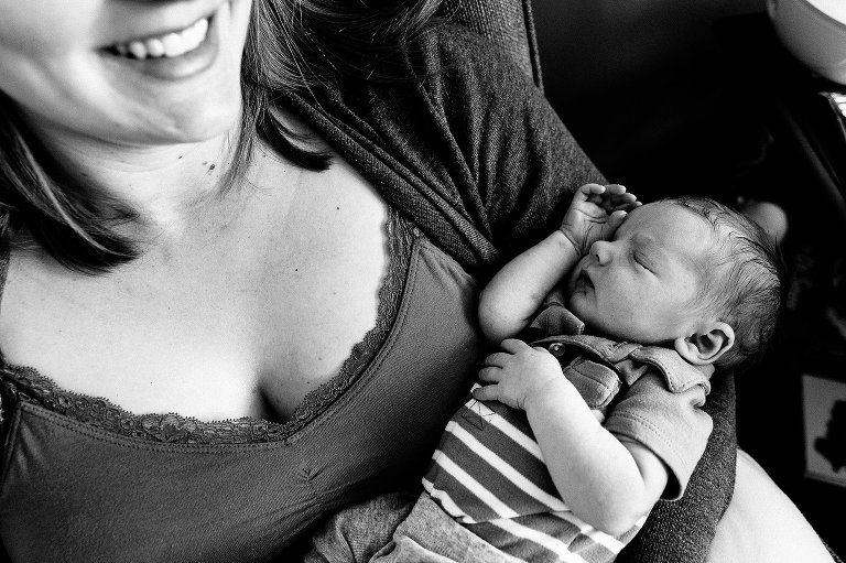 Black and white. Smiling mother holds sleeping newborn. Top-down view. 