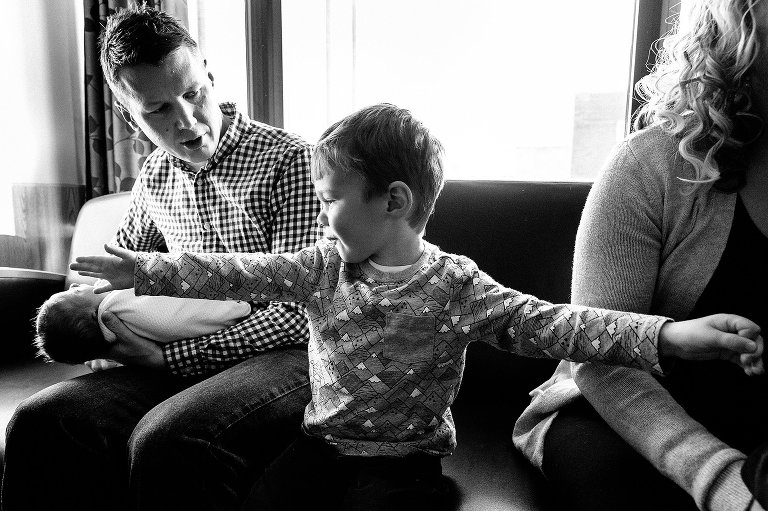 Boy extends arms the entire width of the frame to show how big he is compared to his newborn sister. 
