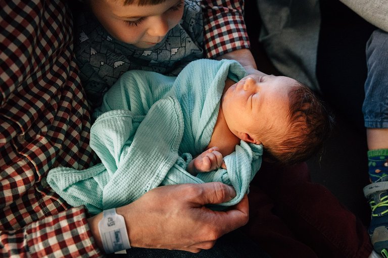 Top down view of big brother and dad looking at newborn details. 