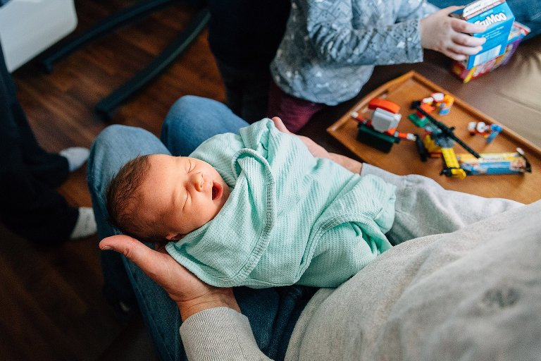 Top down view of newborn being help by grandfather at the hospital. Other grandchildren in the frame. Newborn is yawning. 
