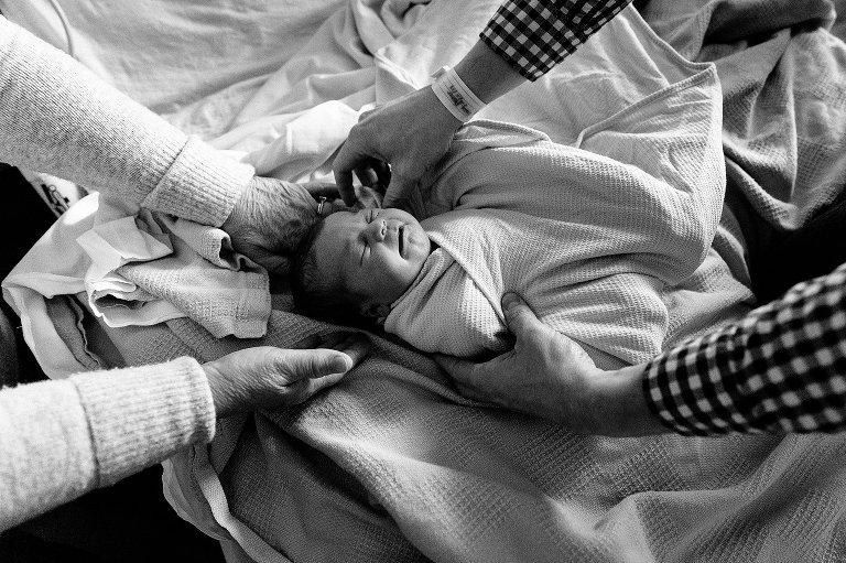 Grandma holds newborn daughter while dad swaddles her. Top down view, black and white. 