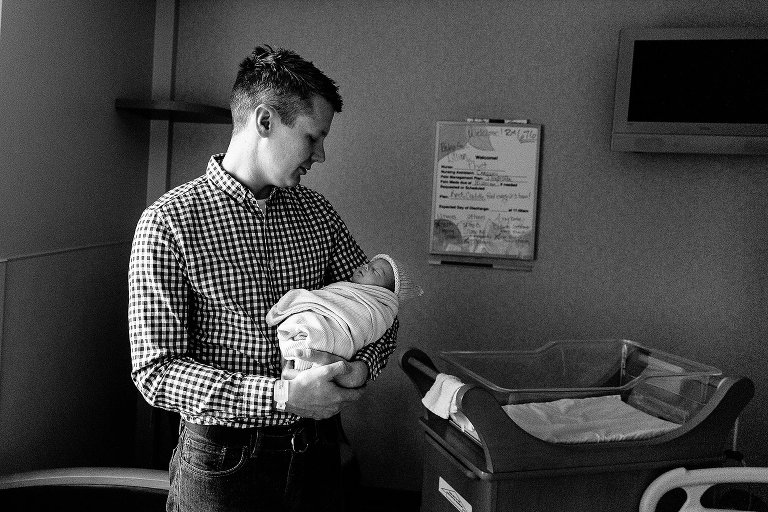 Black and white. Dad holds newborn daughter in hospital room after birth.