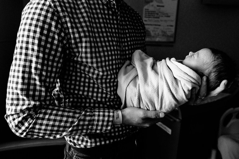 Black and white. Dad holds newborn daughter in hospital room after birth.