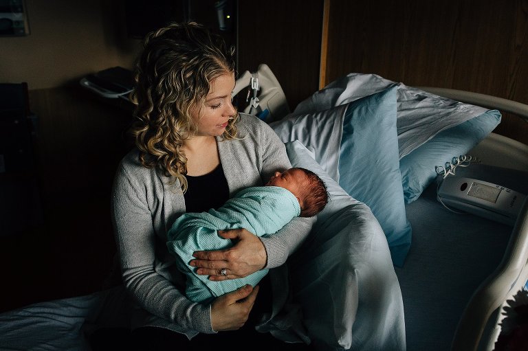 Mother holds newborn baby in arms. Location: hospital room after birth. 
