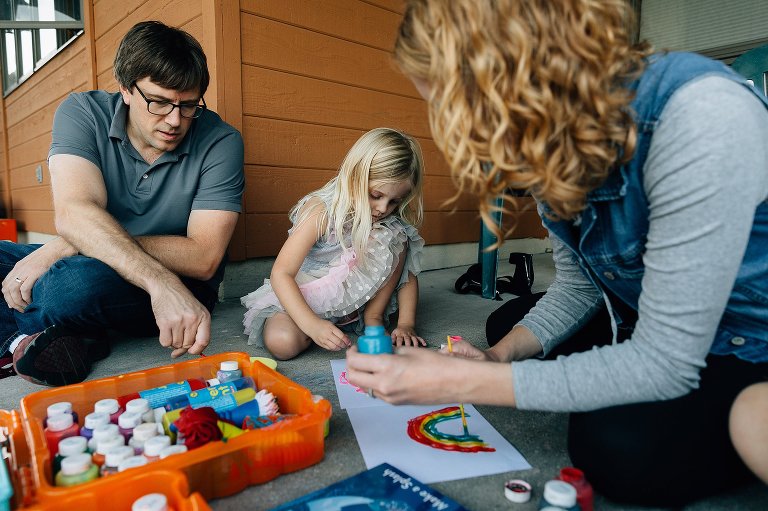 Closer view of youngest daughter painting, framed by both of her parents who are painting.