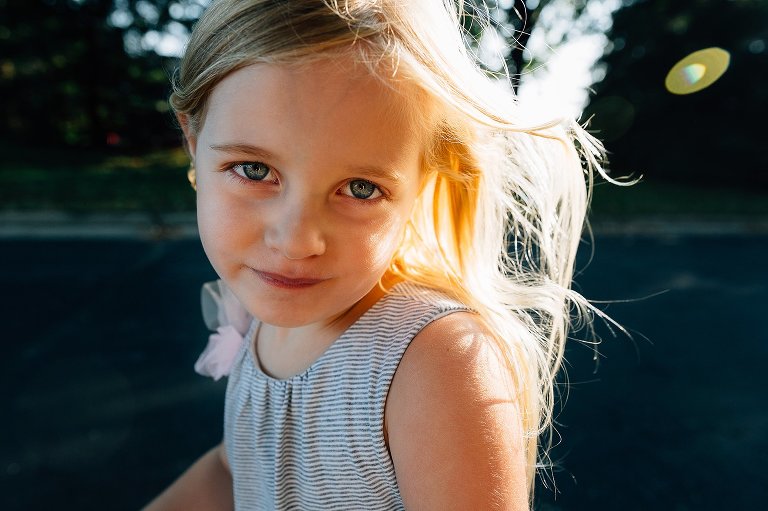 Color. Young girl makes eye contact with camera as the wind from her speed on a scooter blows her hair in the sunshine.