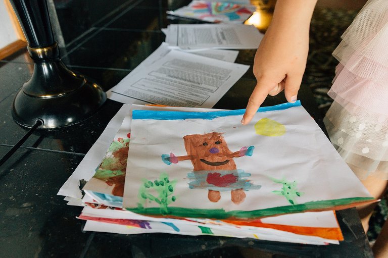 A finger points to a stack of child watercolored illustrations.