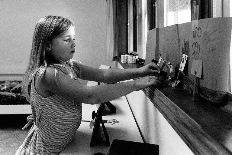 Young girl prepares paper dolls behind a curtain to set the stage for a puppet show