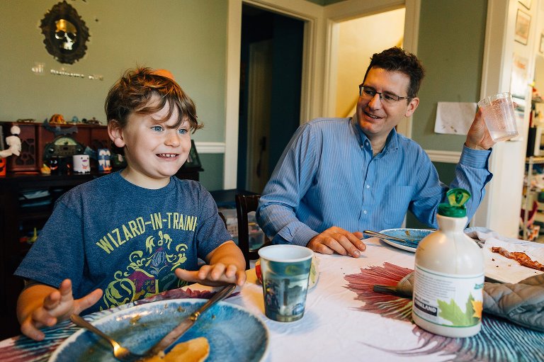 7 year old boy smiles at breakfast while Dad smiles at him. 