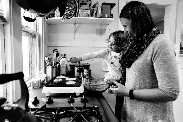Black and white. Mom and girl at the electric griddle. Girl pour pancake batter on the griddle. 