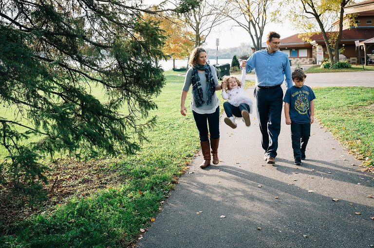 Family of four walks away from lake. Mom and Dad swing daughter in their arms, while Dad engages with son. 