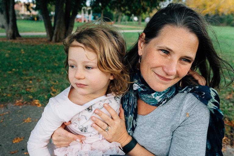 Mom holds girl and is smiling at son off camera. 