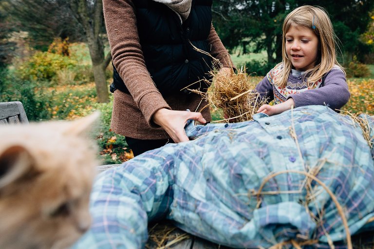 Girl and mom stuff a scarecrow with straw.