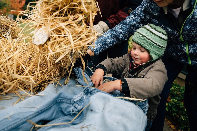 A preschool boy stuffs a pair of jeans with straw to make a scarecrow. 