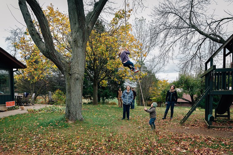 Girl climbs tall rope in backyard as family watches. 