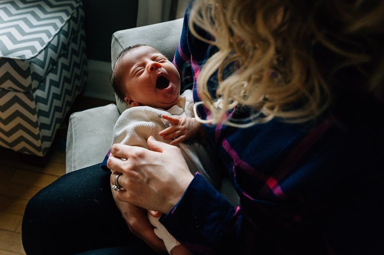 Mother holds sleepy newborn in her arms, newborn is yawning. 