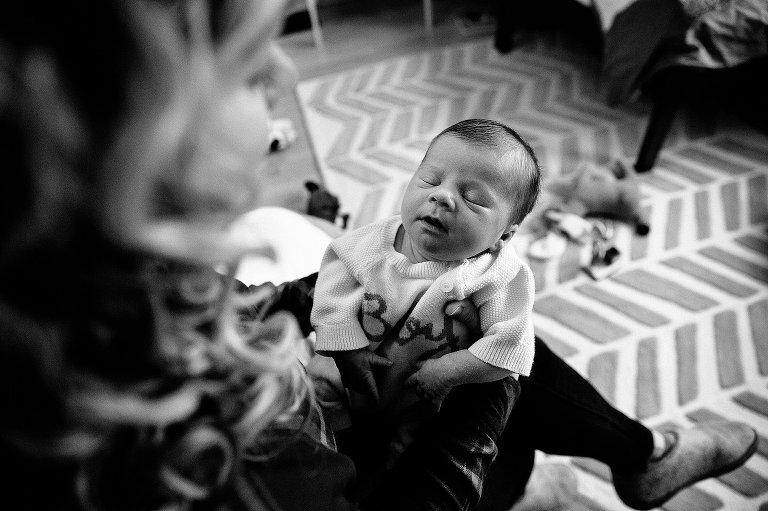 Black and white. Mother holds up sleeping newborn child in older boy's bedroom. 