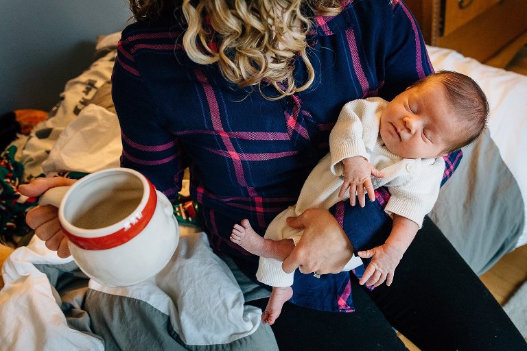 Color. Mother holds newborn girl in one hand and coffee mug in the other. 