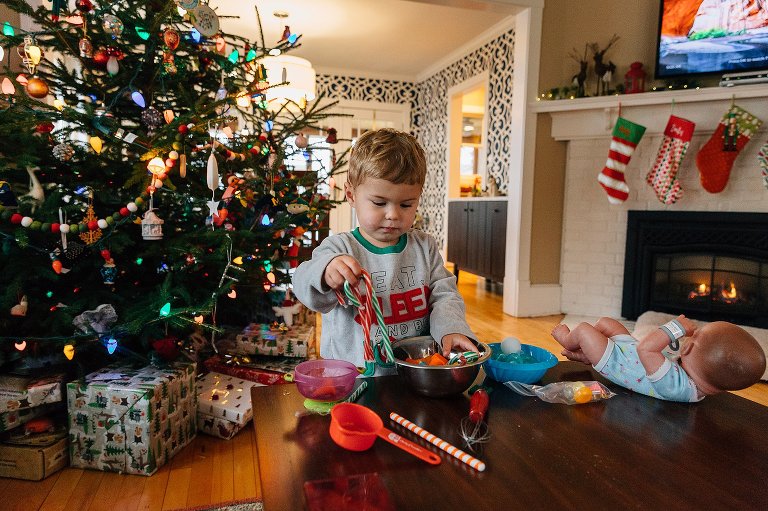 Young boys sorts toys and candy canes on a coffee table. Christmas tree, fireplace wiht stockings and roaring fire in the background. 