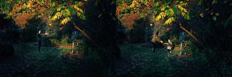Mother holds arms out as she plays with young daughter in the trees with sun light shining on them.