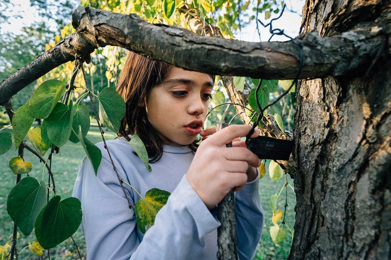 Kid standing outside next to tree looking at tree bark.