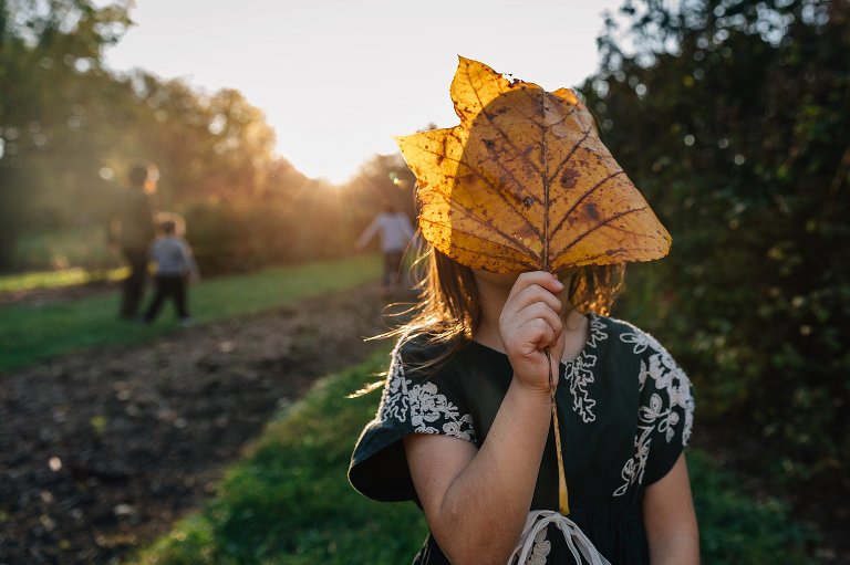 Little girl holds up a giant leaf. Family walking in the background.