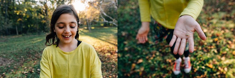 Kid wearing yellow sweater holds up hand with green bug in it. sun setting and colorful fall leaves laying on the green grass.