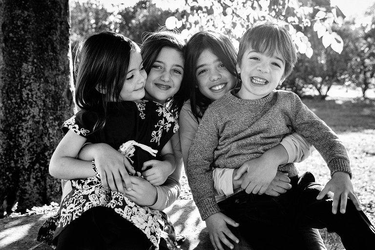 Black and white. Four siblings sit together outside on each others laps.
