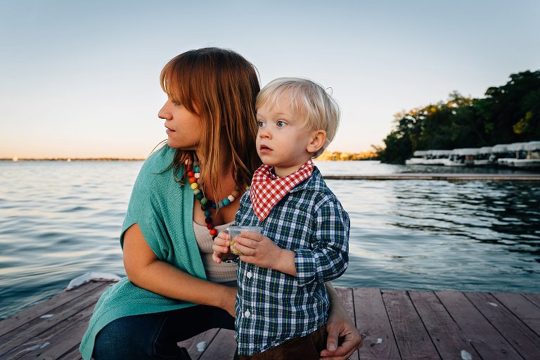 Mother kneels down next to young son on dock over a lake.