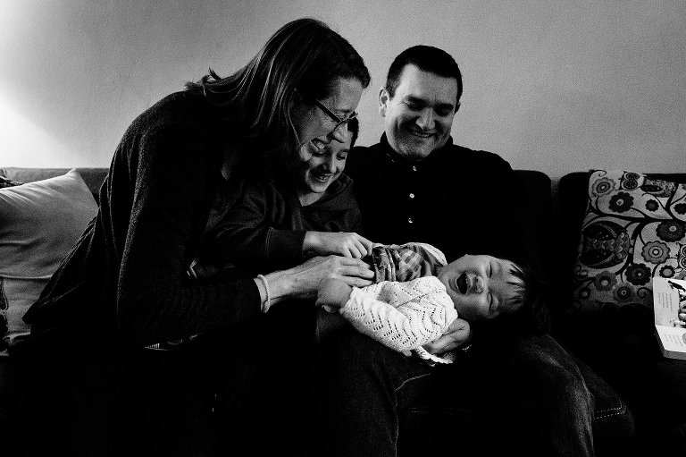 Black and white. Mother father son all sit around youngest son tickling him.