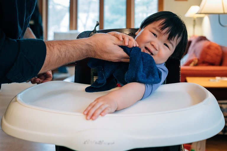 Father uses washcloth to wipe down sons face after eating breakfast.
