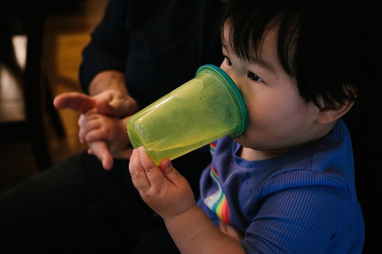 Father holds young sons hand while he drinks from sippy cup.