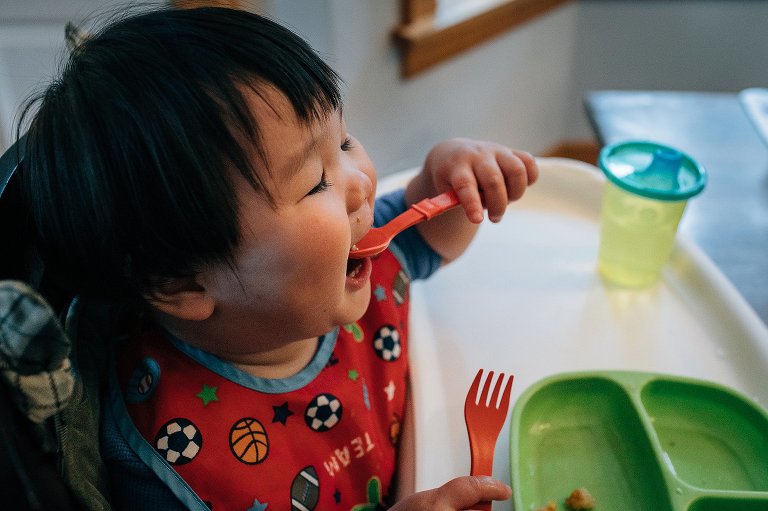 Little boy sits in highchair eating breakfast.