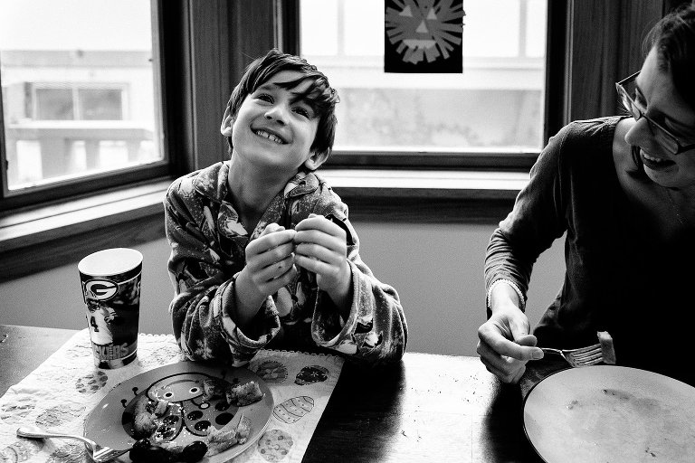 Black and white. Family eats breakfast together at dinning room table.