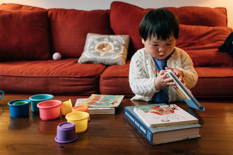 Little boy sitting in living room plays with staking cups and picture books.