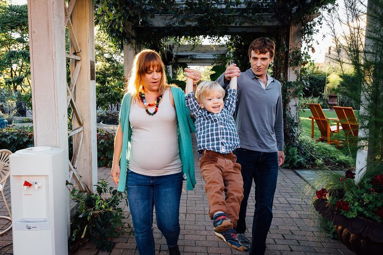 Dad and pregnant mom walk down path swinging toddler in the air.