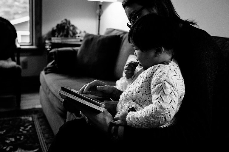 Black and white. Little boy sitting on mothers lap reading picture book.