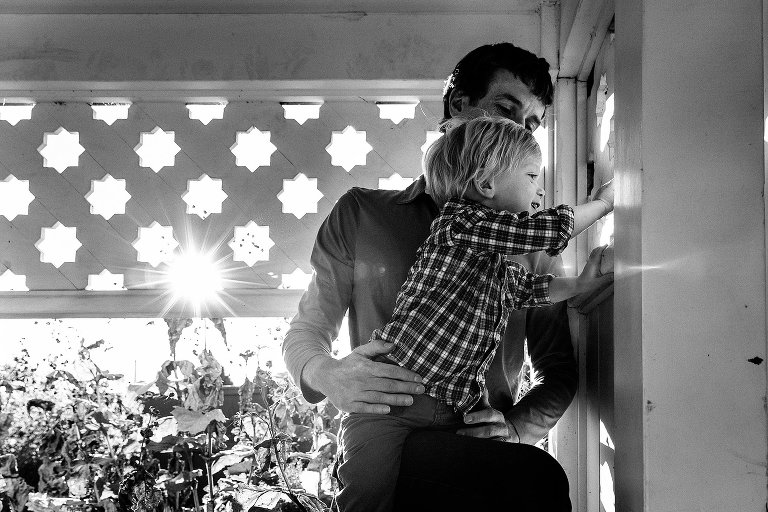 Black and white. Father holds up little boy looking at garden.