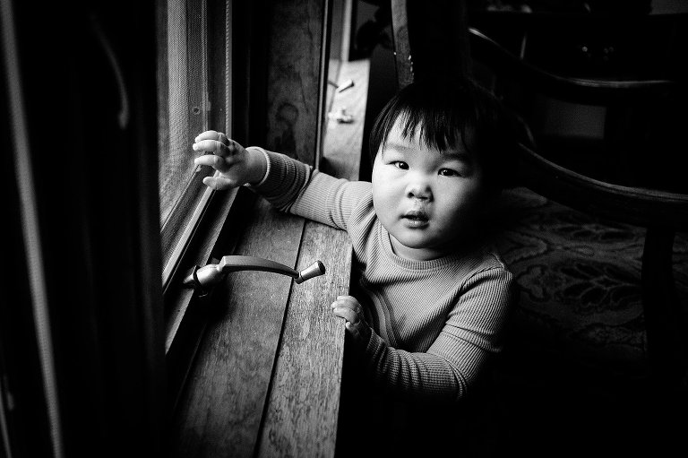 Black and white. Little boy standing and looking out of window.
