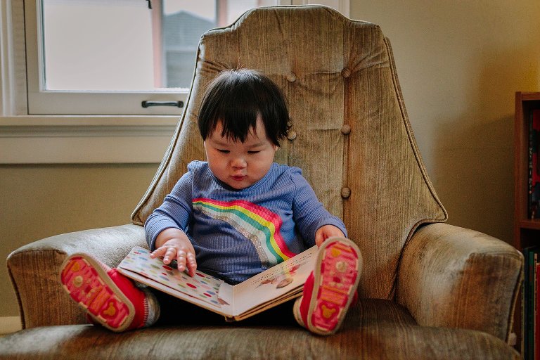 Little boy reads picture book while sitting in rocking chair.