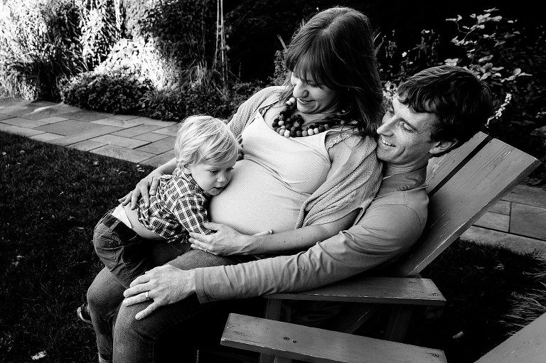 Family all sitting on outdoor chair. son hugging pregnant mothers belly.
