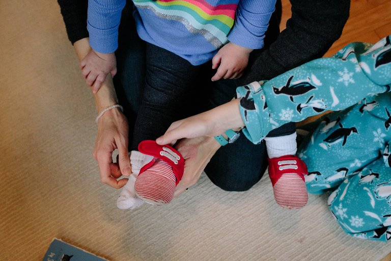 Mother puts little shoes onto sons feet. older brother helps his mom.