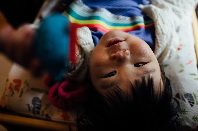 Little boy laying down looking up at camera.