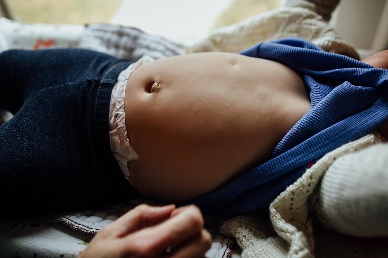 Little boy laying down lifts up shirt showing bellybutton.